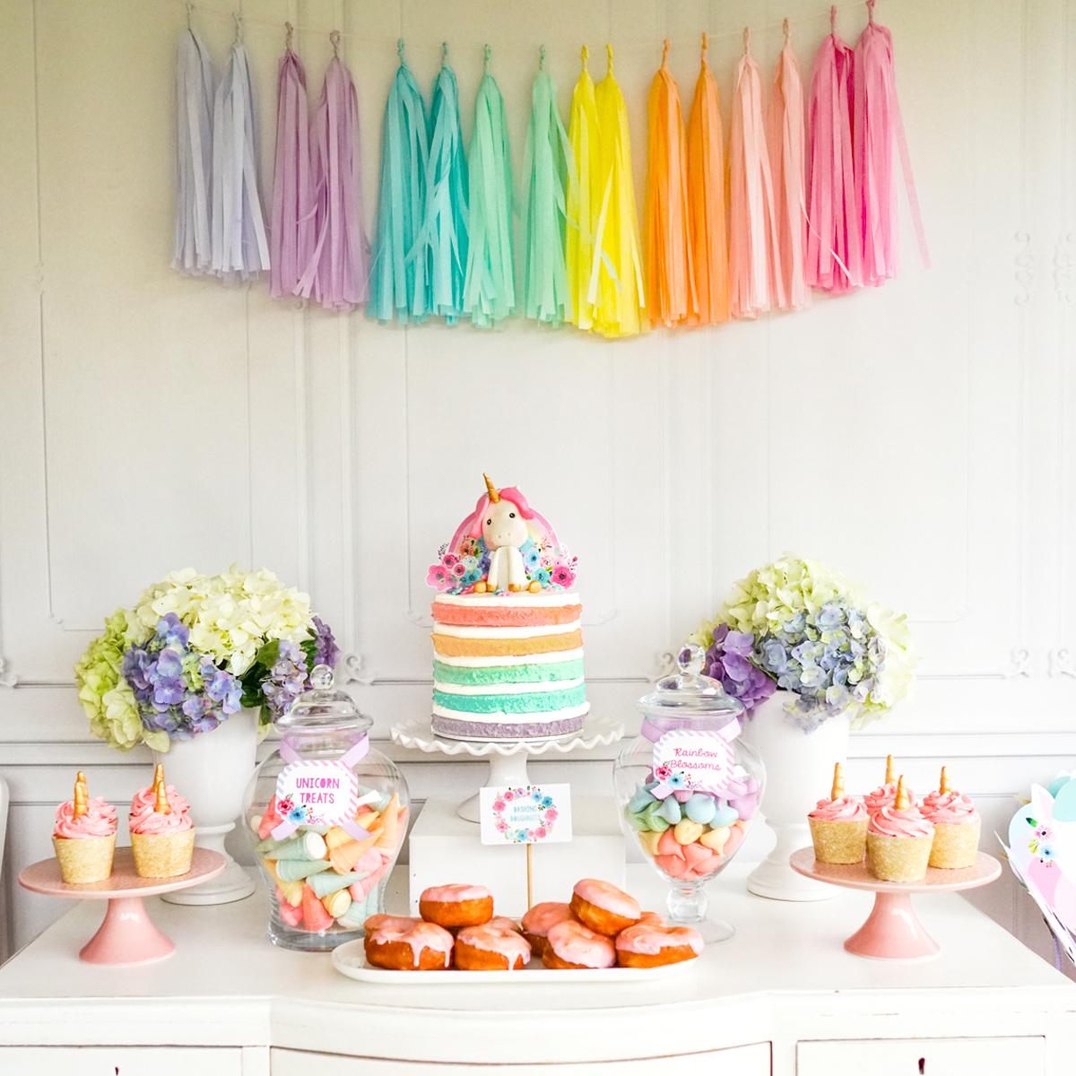 Pretty pastel unicorn party dessert table set up with rainbow colored sponge rainbow cake.